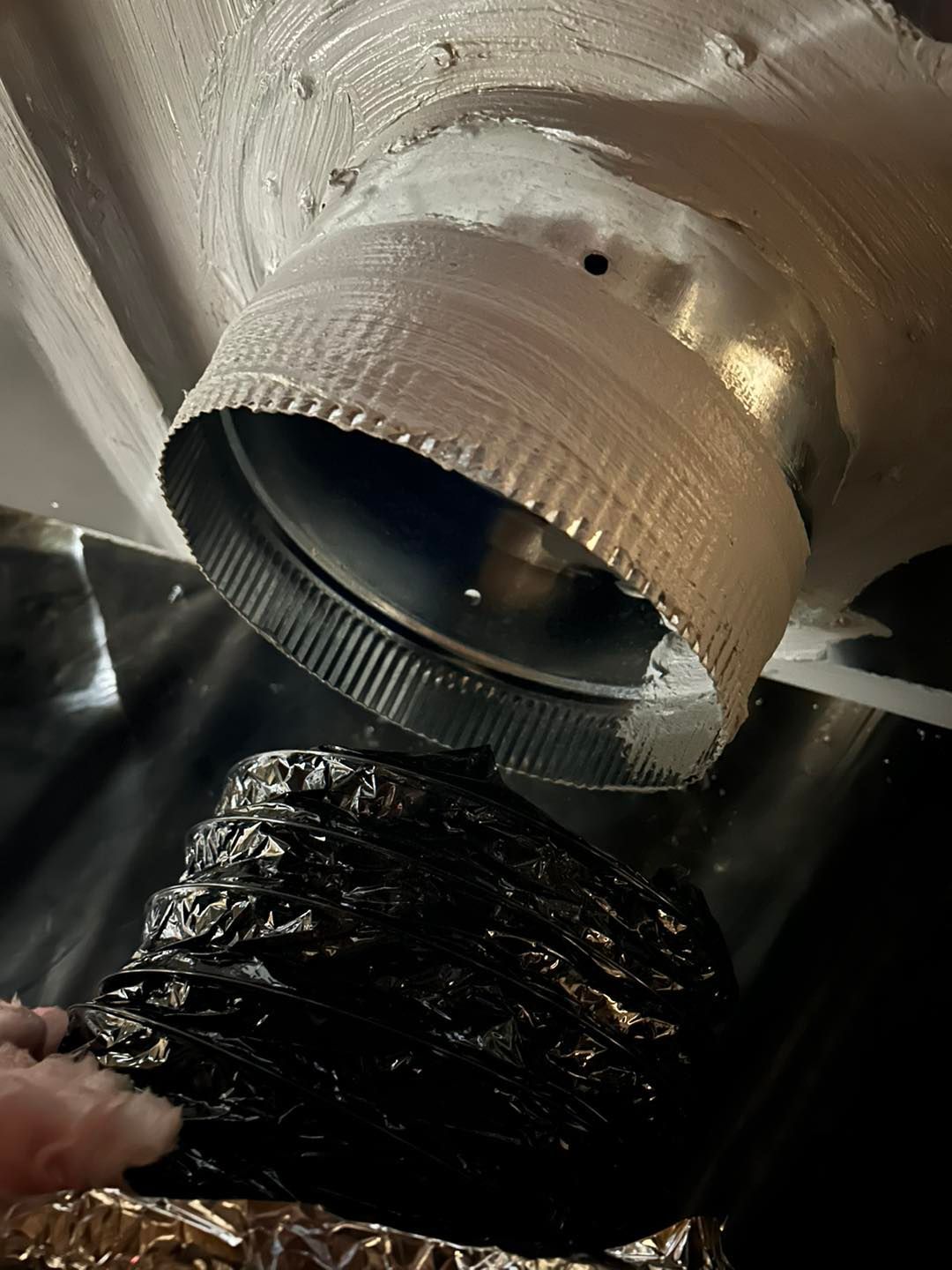 A person is holding a piece of black plastic next to a metal pipe.