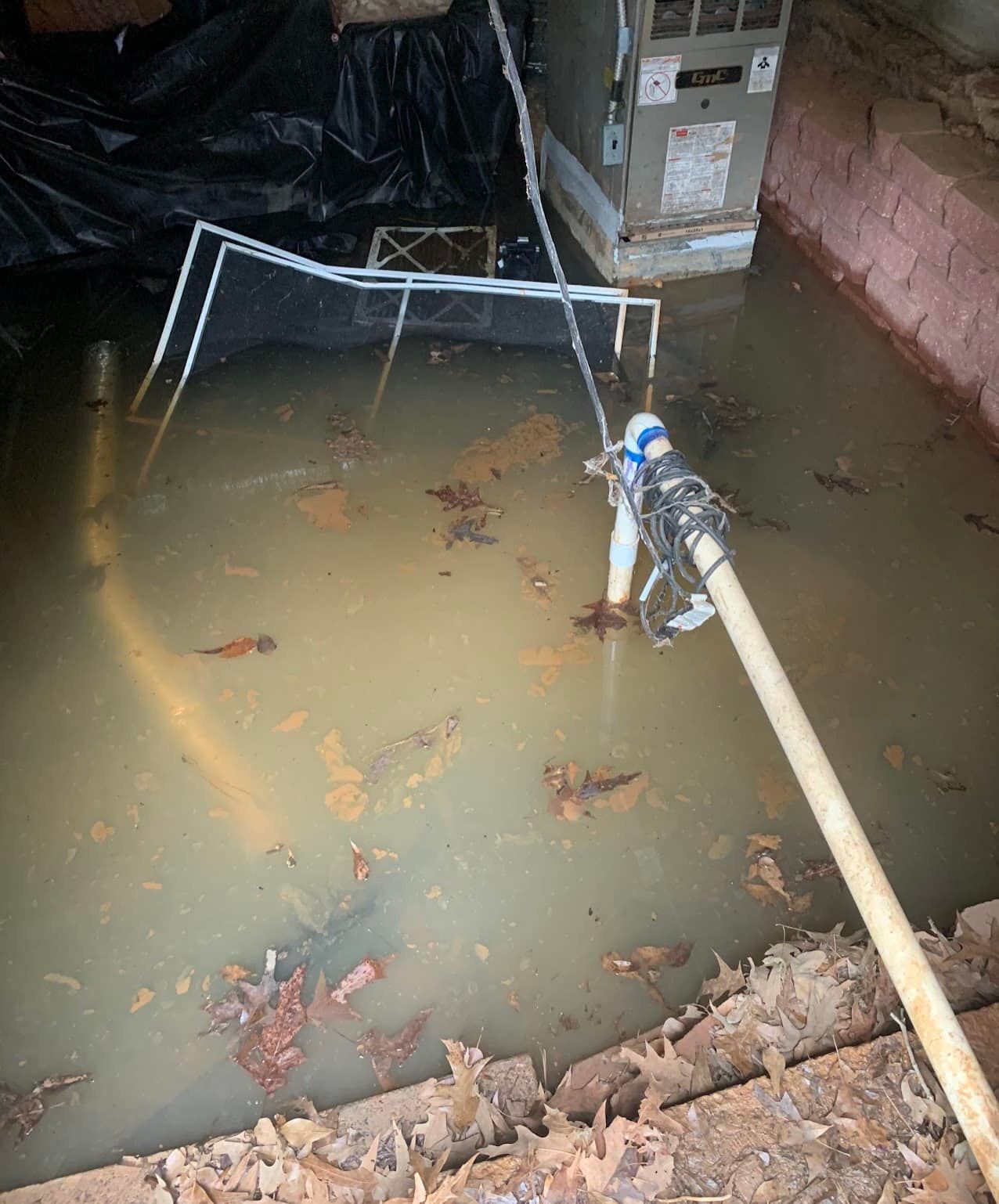 A hose is hanging from a pipe in a flooded basement.