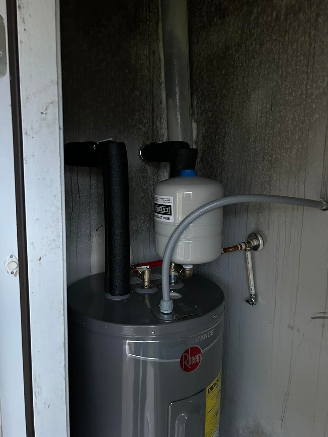 A water heater is sitting in a dirty room next to a door.
