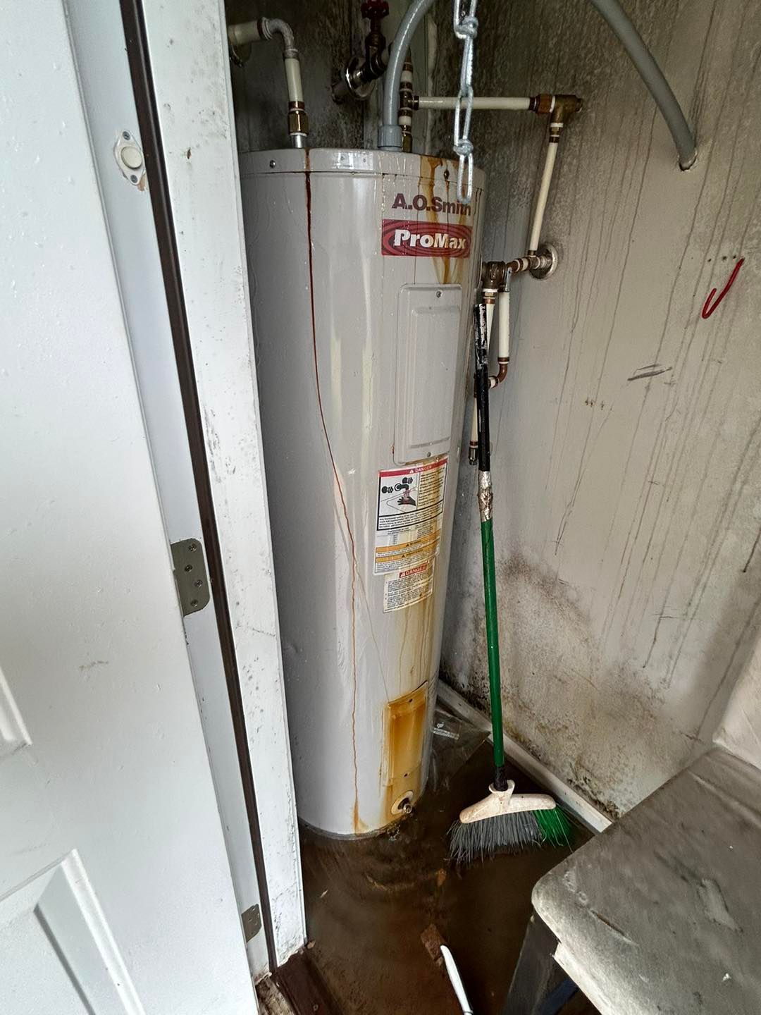 A water heater is sitting in a dirty room next to a door.