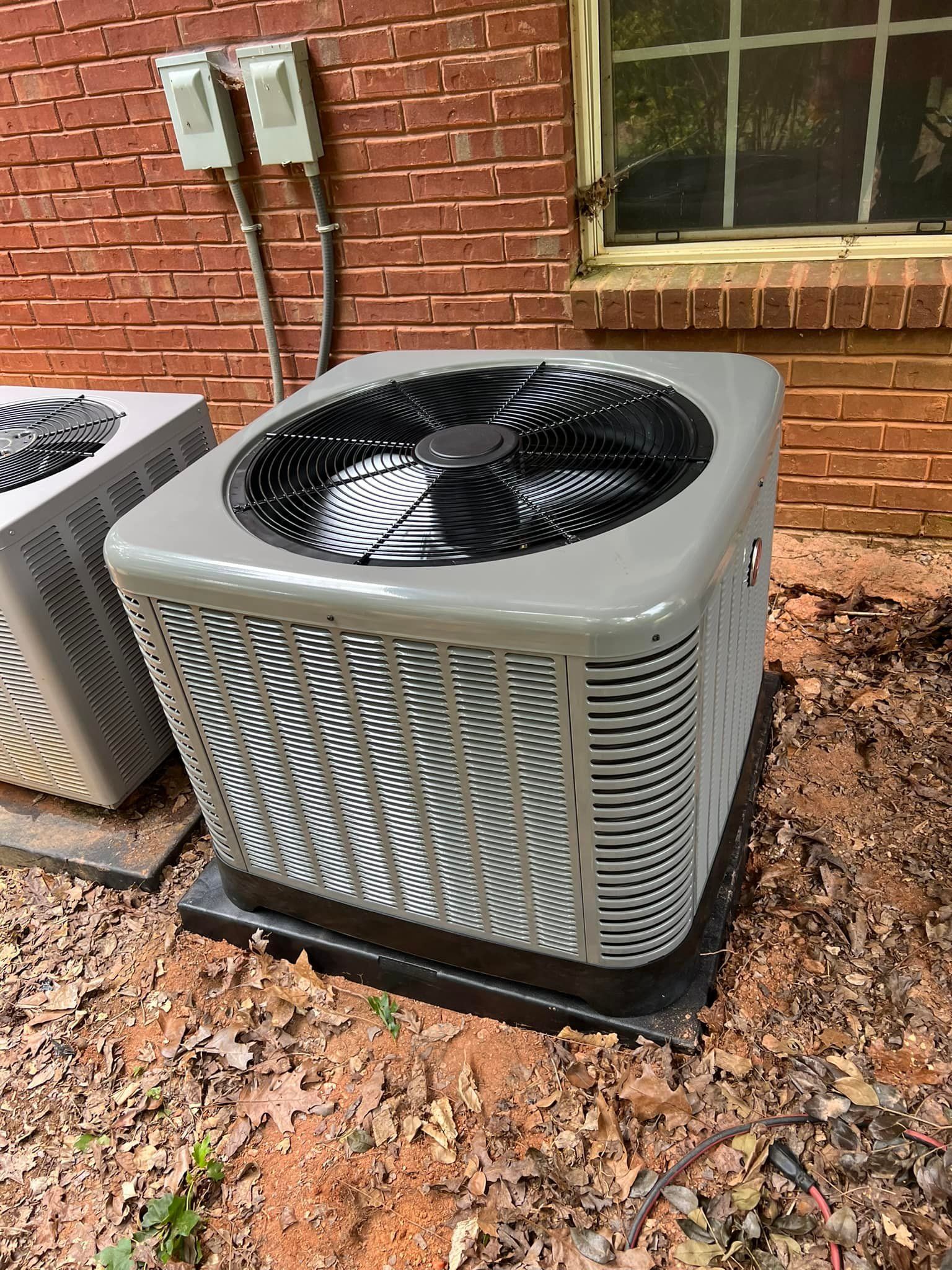 A large air conditioner is sitting on the ground in front of a brick building.