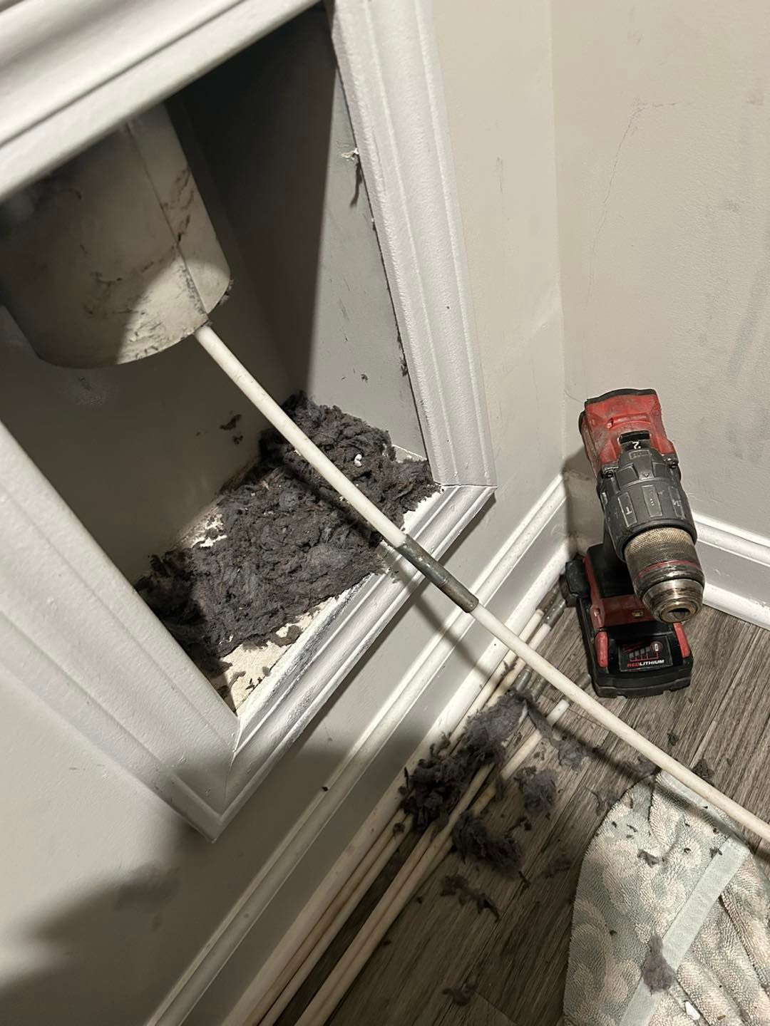 A drill is sitting in a corner of a room next to a mop.