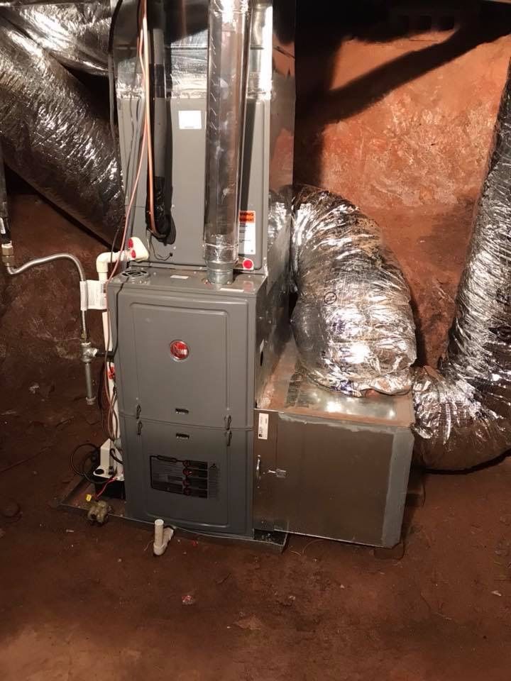 A furnace is sitting in a basement next to a bunch of ducts.