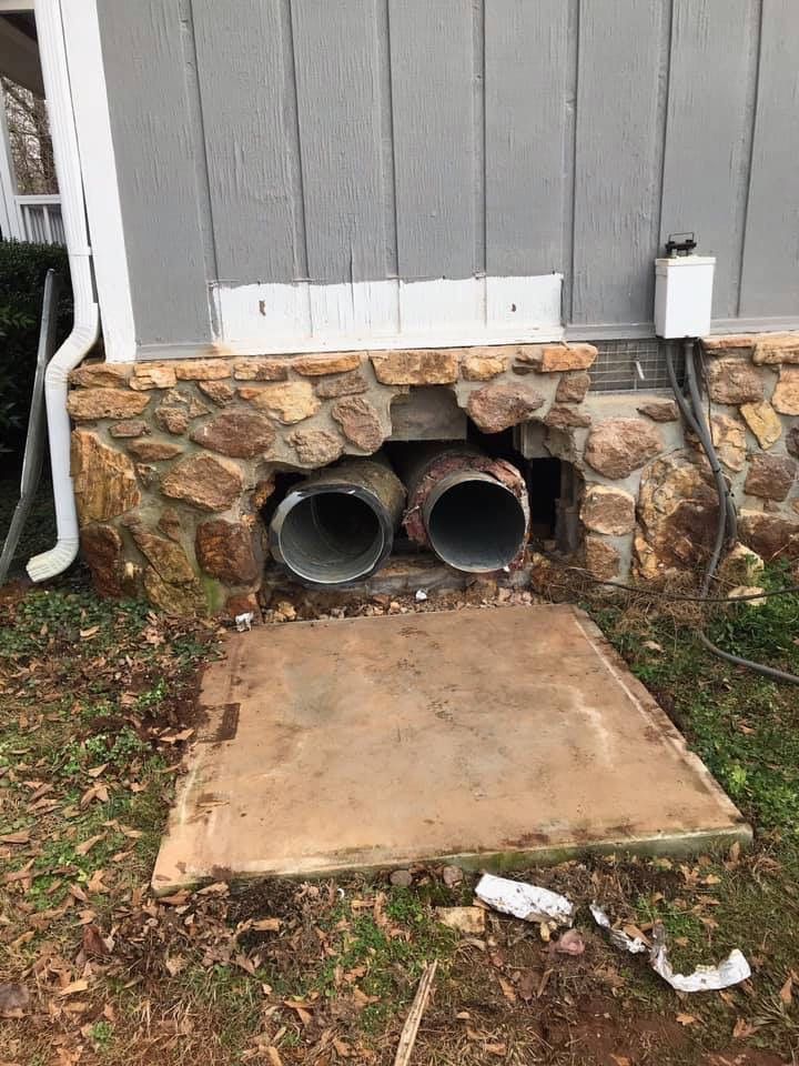 Two pipes are coming out of a hole in the side of a house.