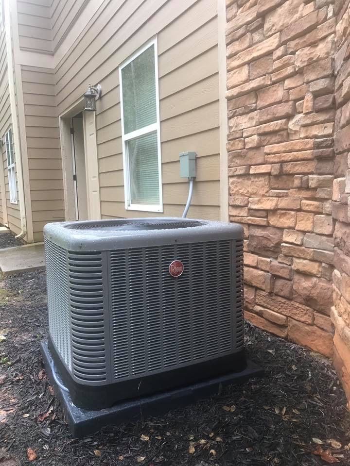 An air conditioner is sitting outside of a house next to a window.