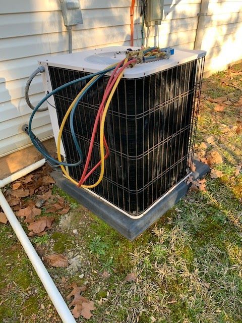 An air conditioner is sitting outside of a house with hose attached to it.