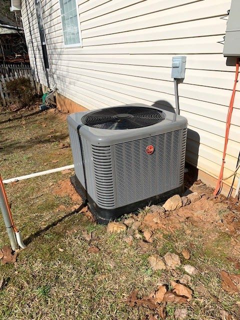 A gray air conditioner is sitting on the side of a house.