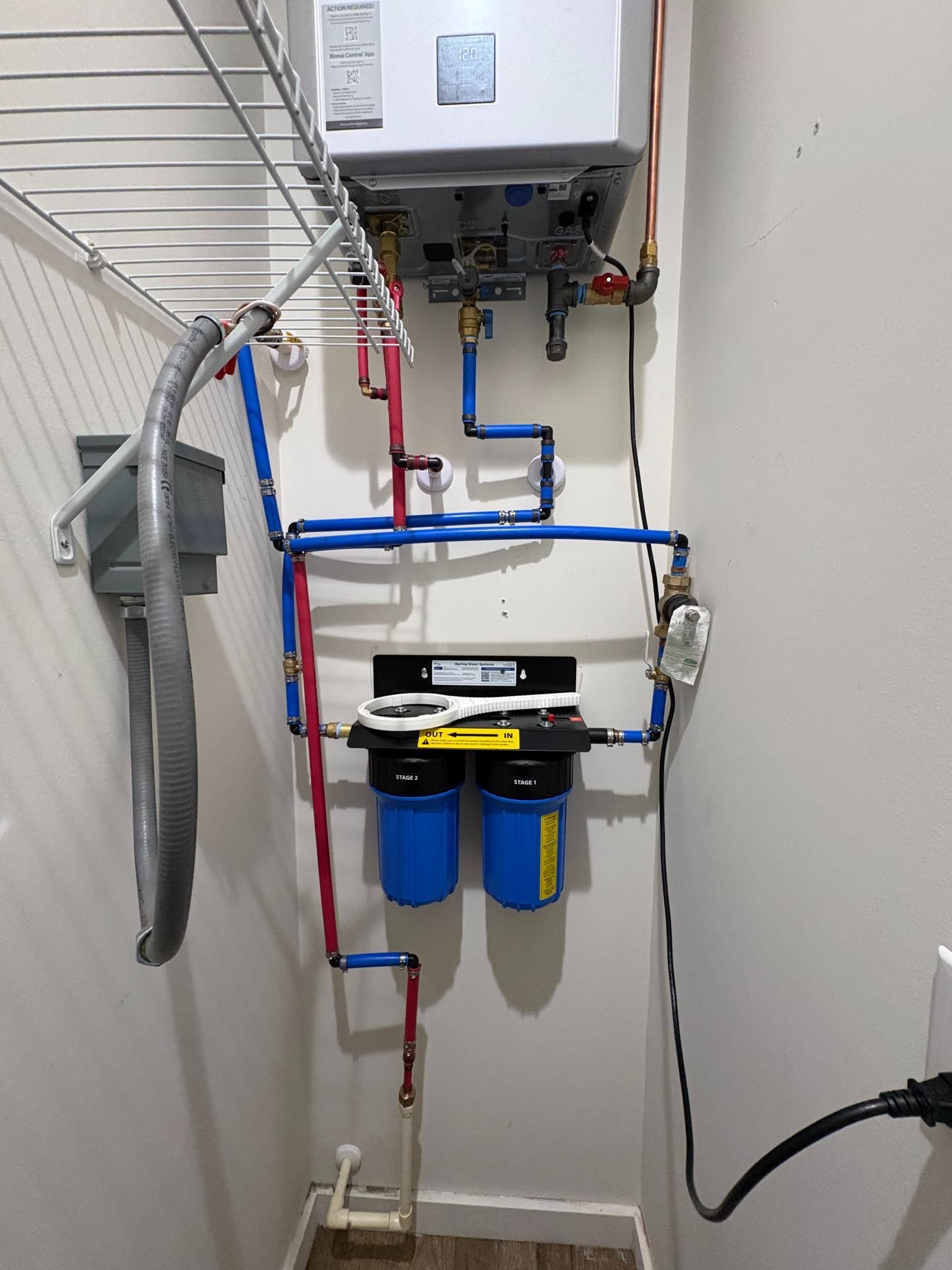 Wall-mounted water filtration system with blue and red pipes and dual blue filters in a utility room
