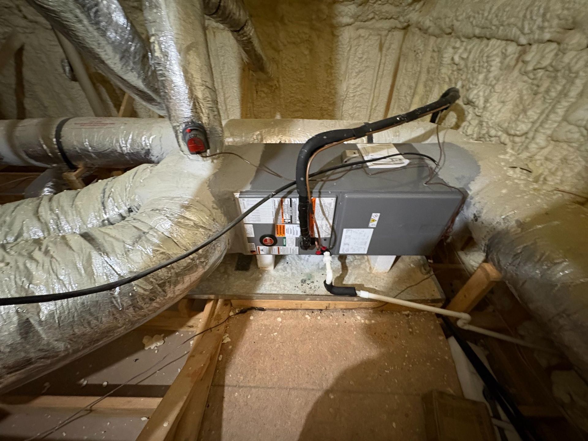 Attic HVAC unit and ductwork wrapped in insulation, with exposed floor joists and wiring