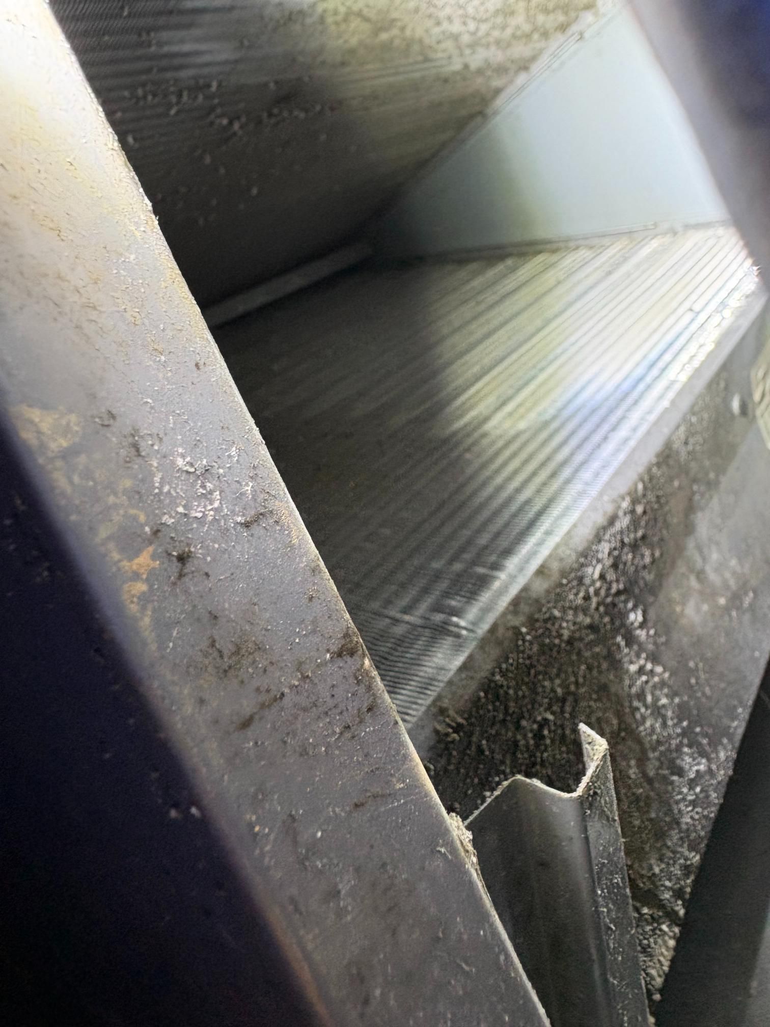 Dusty metal air duct interior with slanted ridged panel and dark frame edges