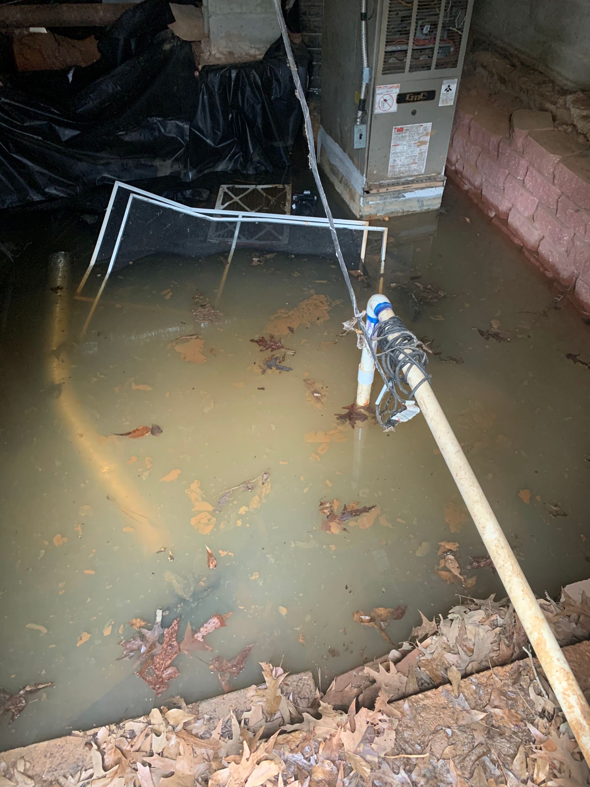 A hose is sitting in a flooded basement next to an air conditioner.