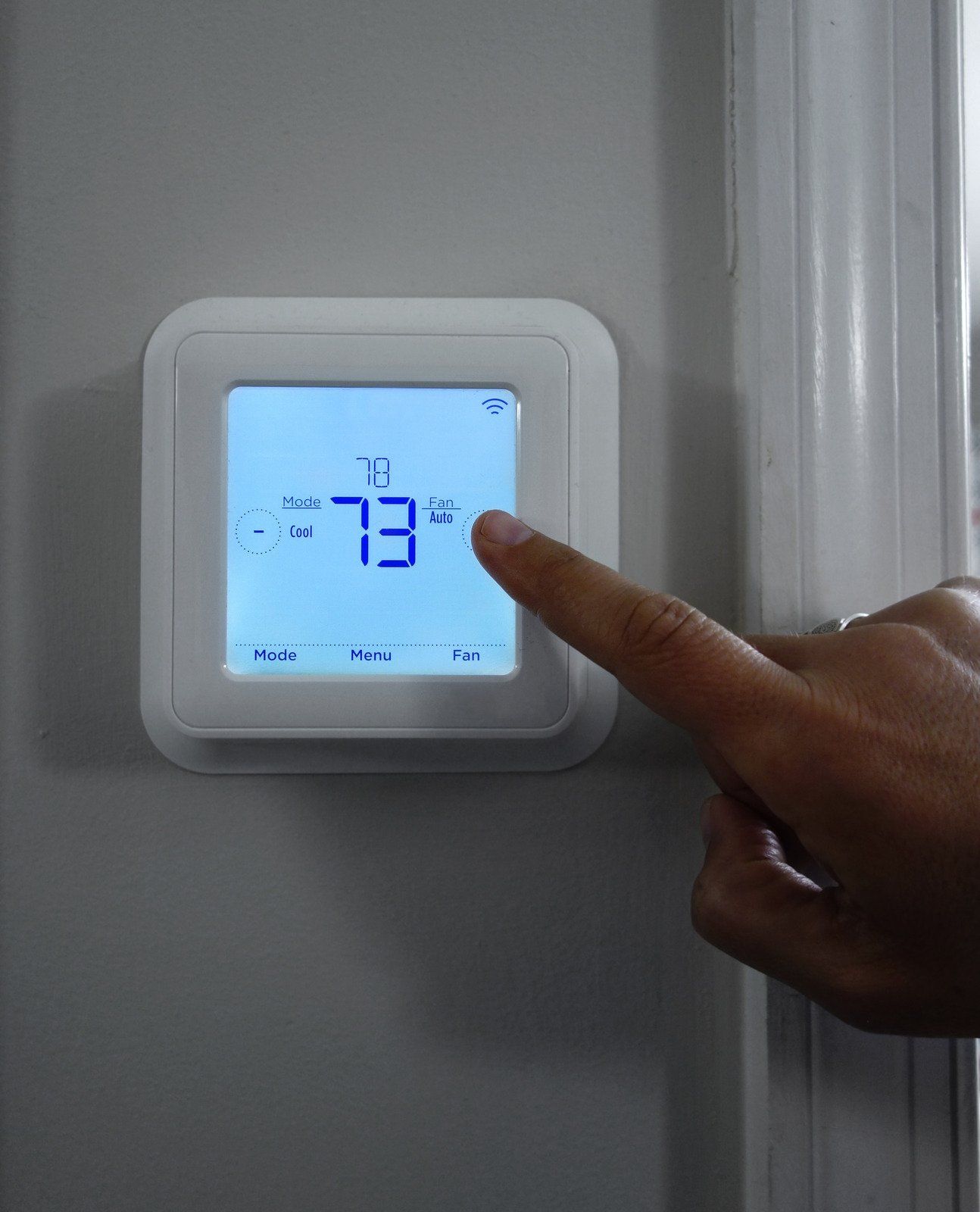 A person is pressing a button on a thermostat that reads 73 degrees