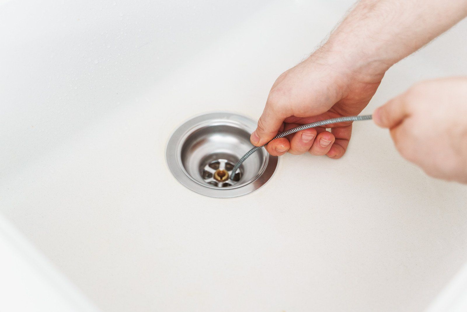 A person is cleaning a sink drain with a spoon.