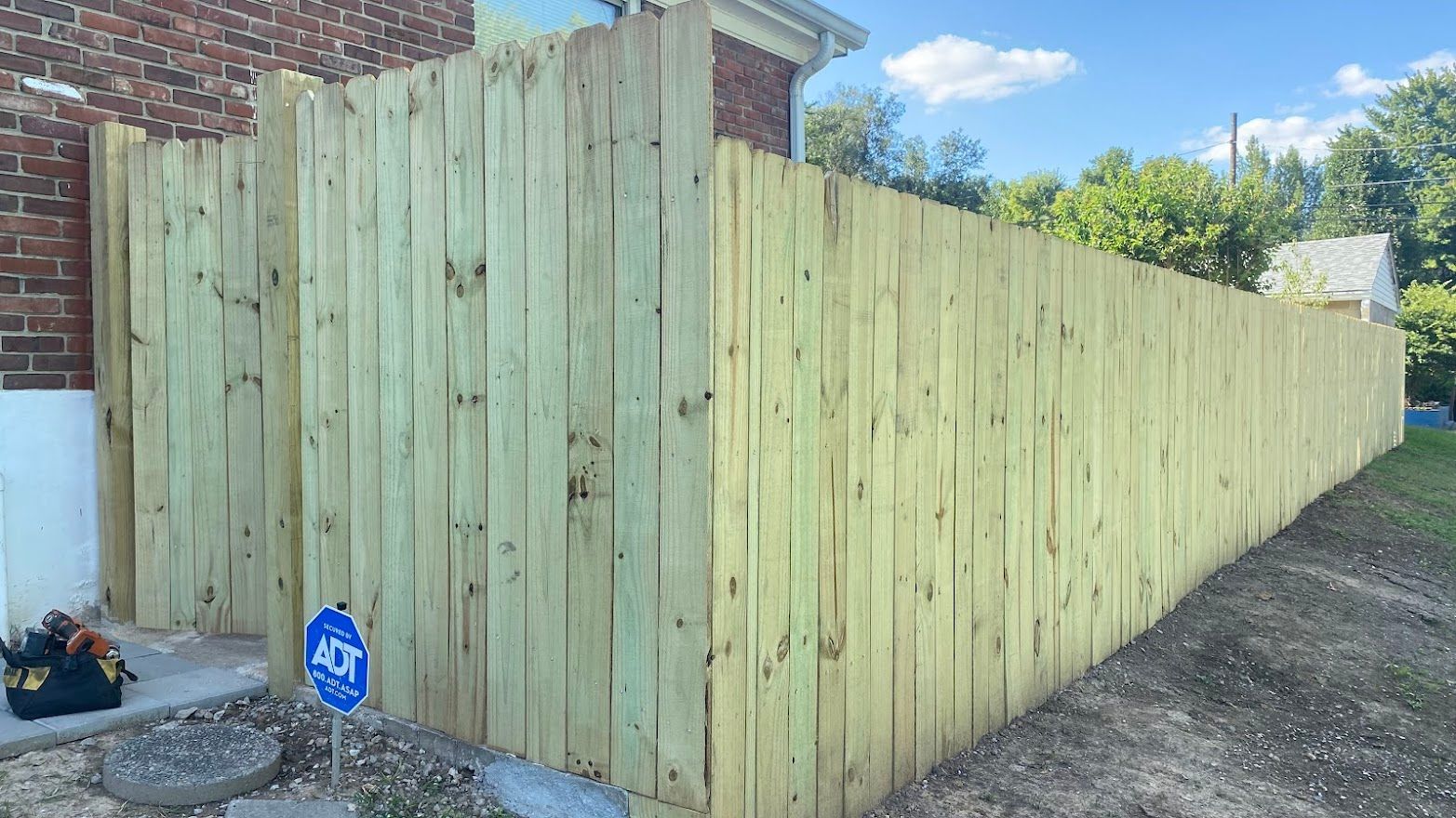 A wooden fence surrounds a yard next to a brick building. The fence is constructed of vertical planks.