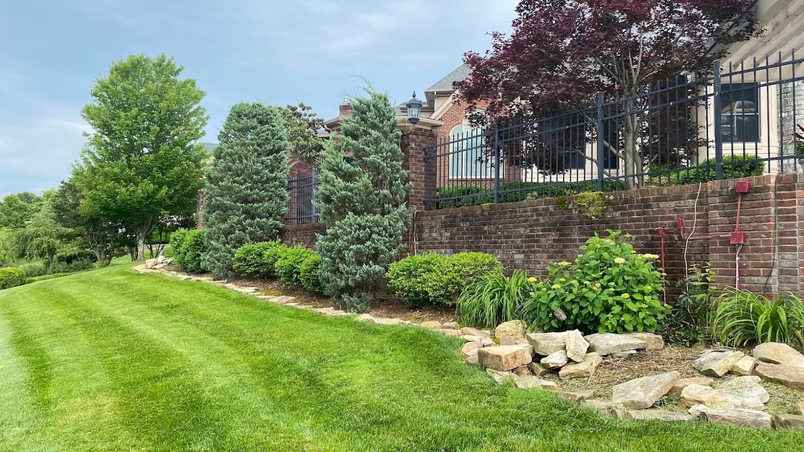 A lush green lawn in front of a house with a brick wall.