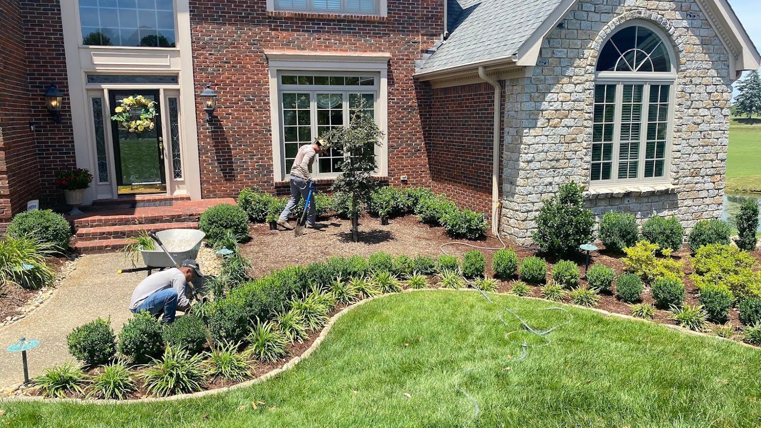 A man is working on a landscaping project in front of a large brick house.