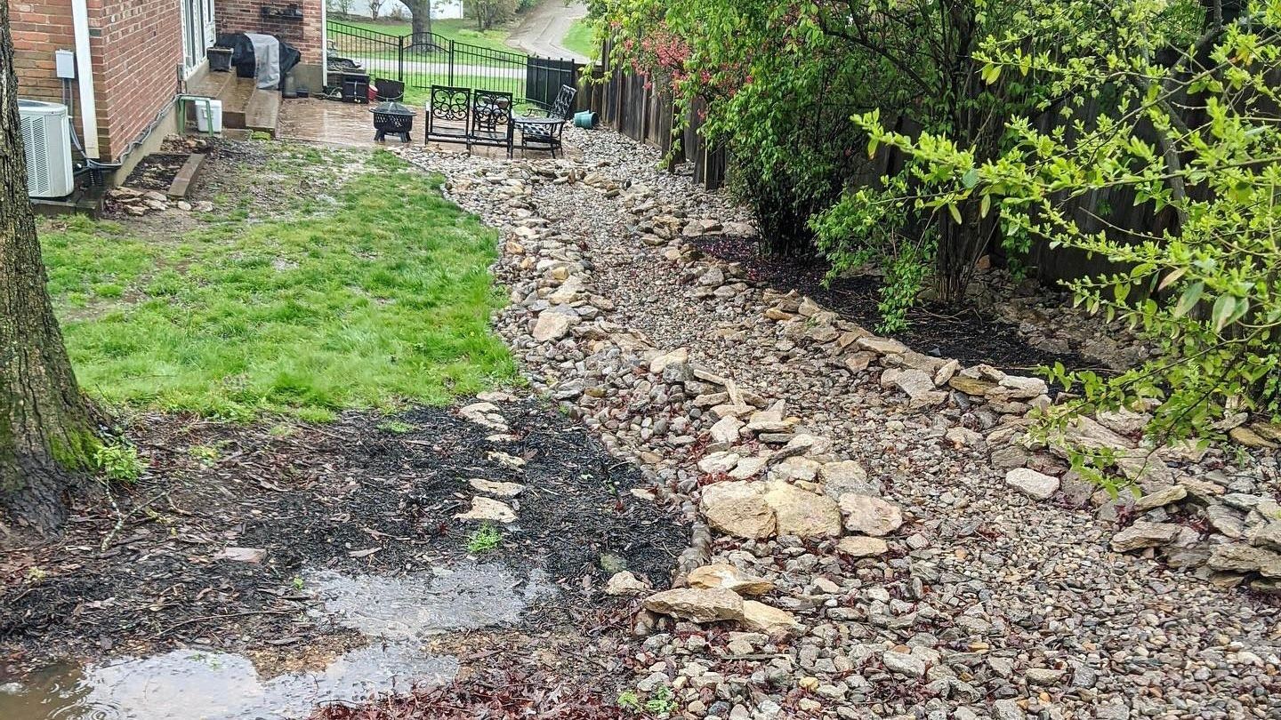 A backyard with a lot of rocks and a puddle of water.