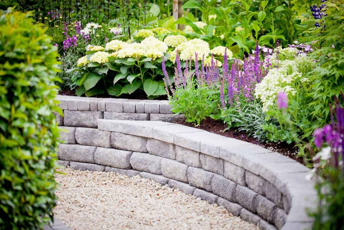 A stone wall surrounded by flowers and gravel in a garden.