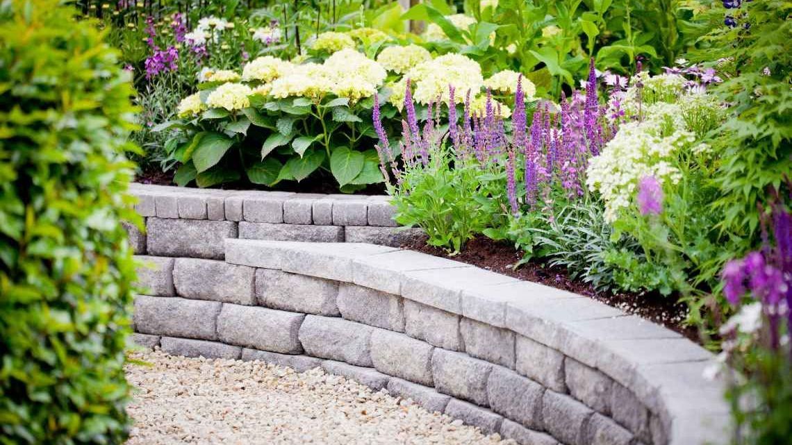 A stone wall in a garden surrounded by flowers and plants.