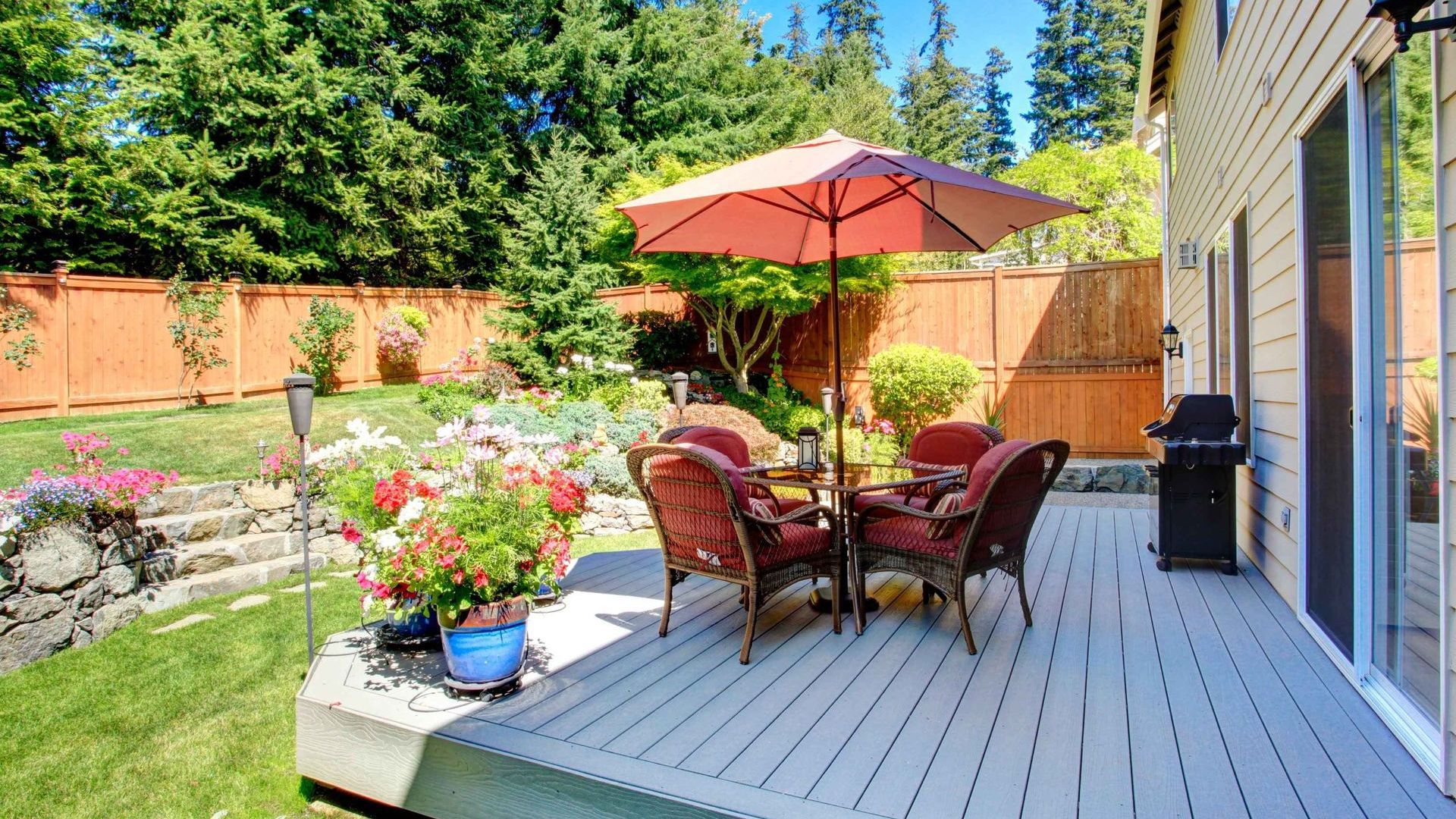 A beautiful backyard, featuring a wooden privacy fence, a slab deck and colorfull flowers and shrubs.