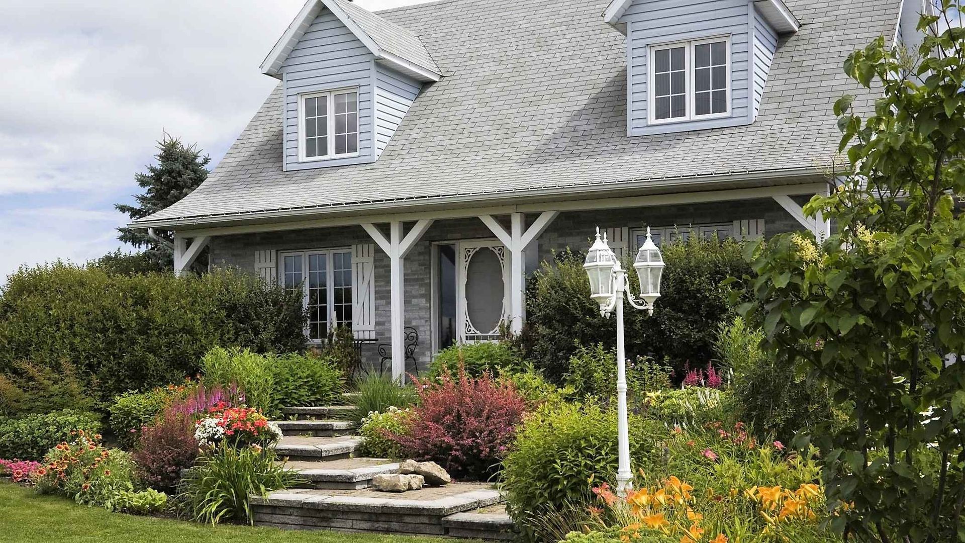 A large house with a porch and stairs surrounded by flowers and bushes.