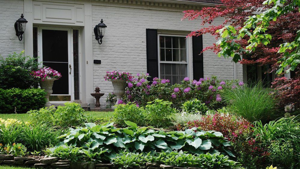 A white brick house with black shutters and a garden in front of it.