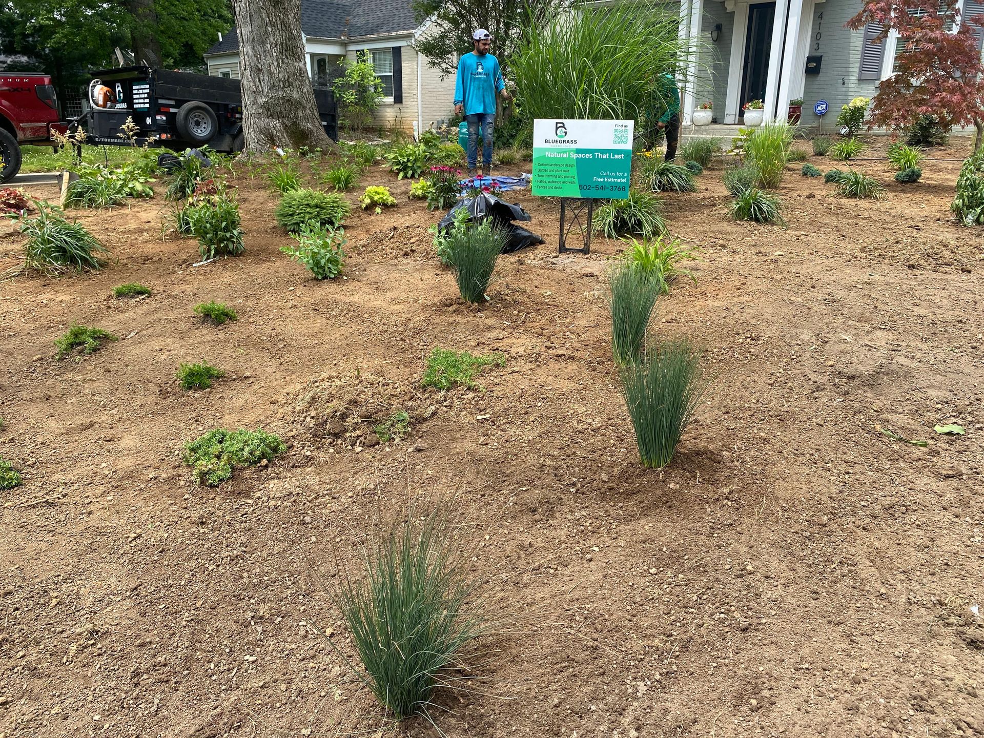 Landscaped bed with colorful plants in front of a brick building and air conditioning units.