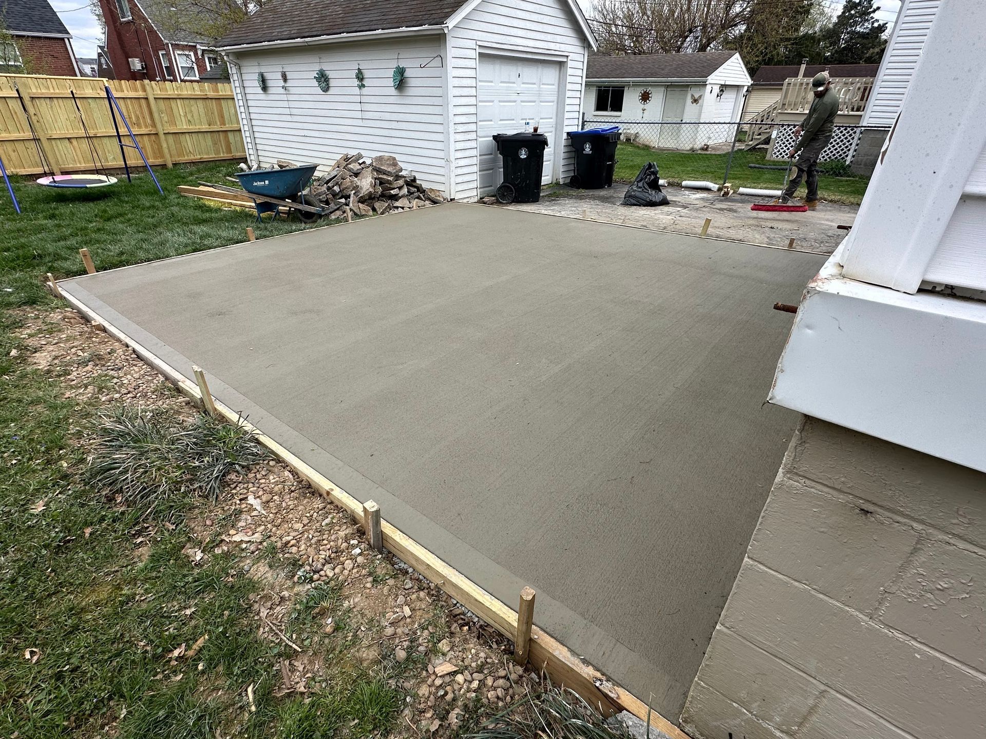 Freshly poured concrete patio with wooden frame in a backyard.