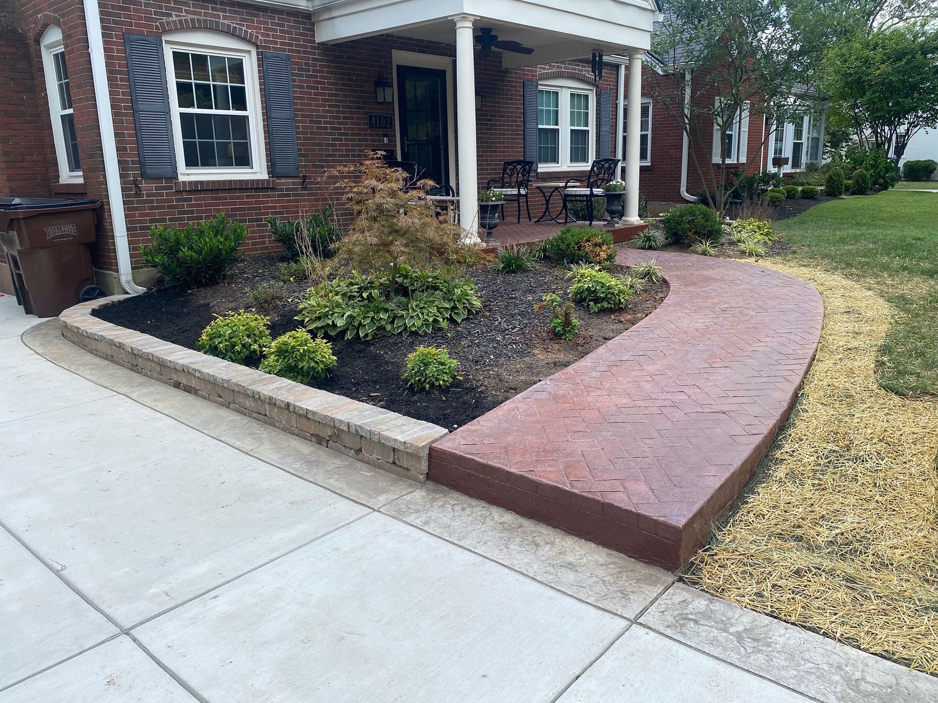 Red brick home with a stamped concrete walkway, garden, and black mulch.