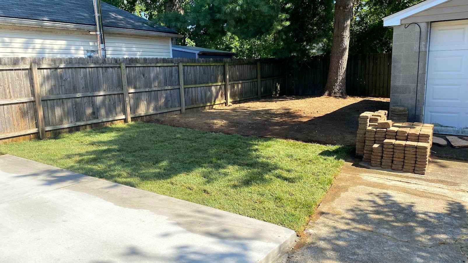 A backyard with a freshly mowed lawn, wooden fence, and a stack of bricks next to a white garage.