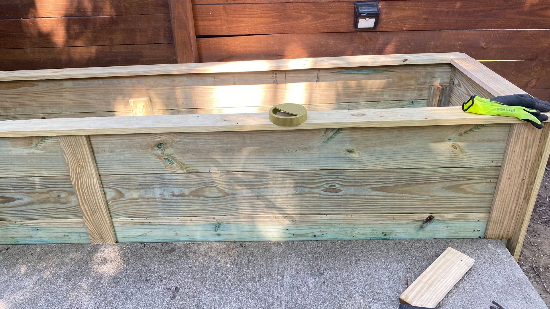 Wooden raised garden bed with weathered planks, tools on top, against a wooden fence.