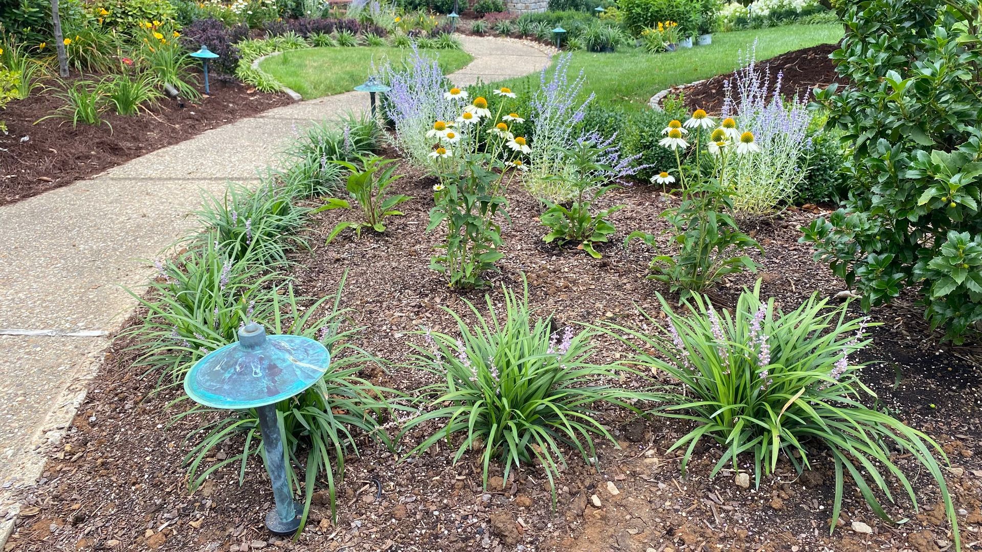 A two-story brick house with a circular turret. Green lawn, garden beds, and trees adorn the front yard.