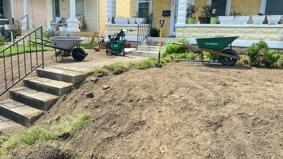 Yard work scene: Dirt pile with steps, wheelbarrows, and tools in front of a house.