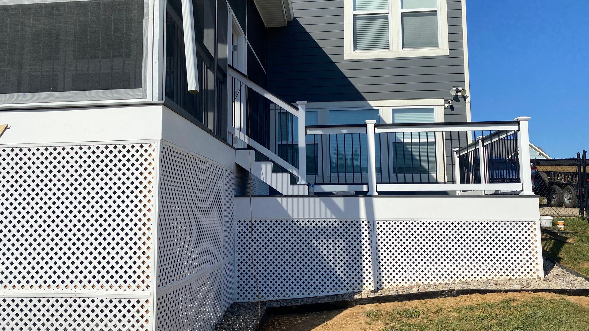 A white deck with lattice skirting and black railings leads up to a house with blue siding.