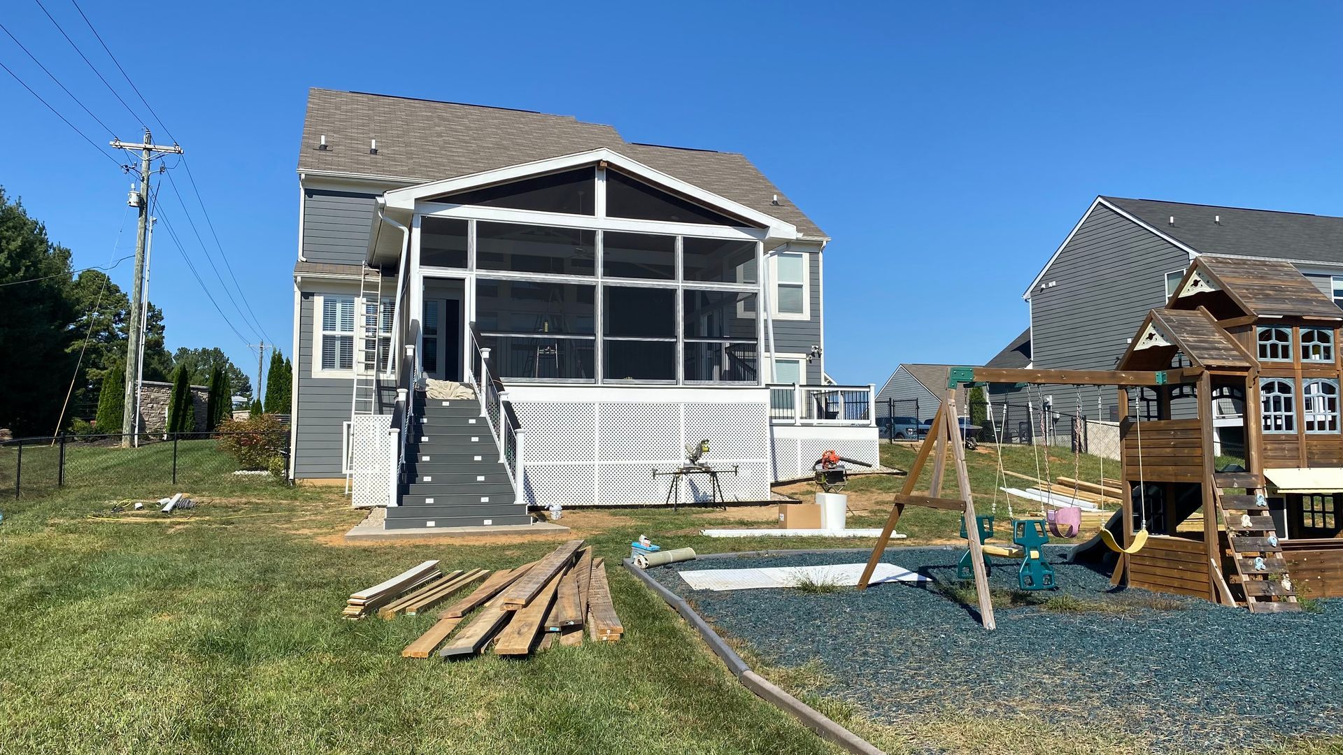 Backyard with a gray house, screened porch, play set, and blue play area on a sunny day.