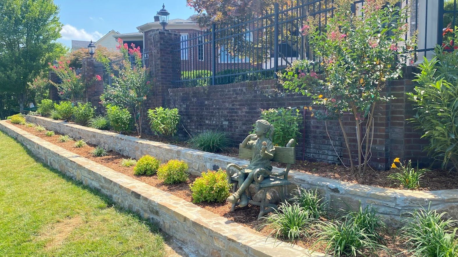 A brick wall surrounds a lush green yard with a statue in the middle of it.