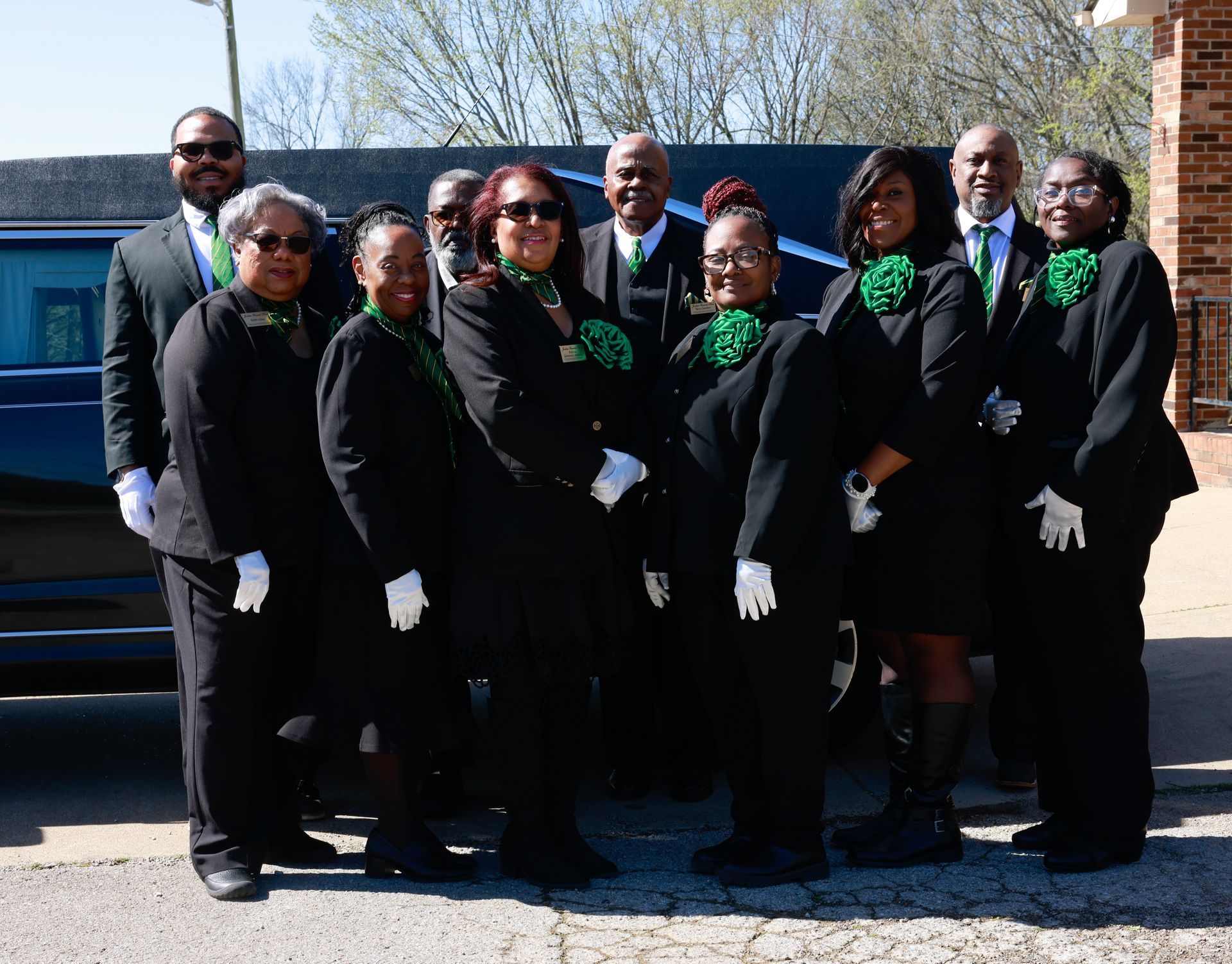 Group of formally dressed people posing outdoors beside a blue vehicle.