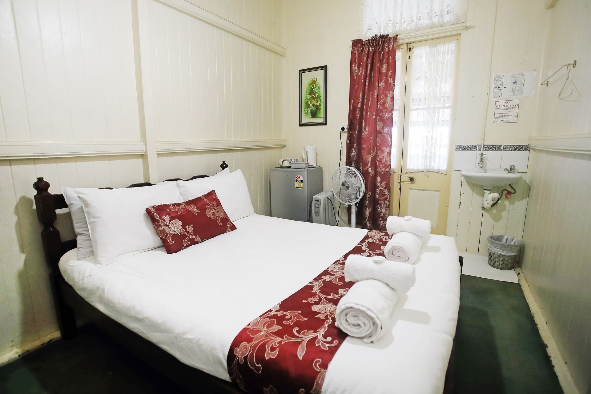 Bedroom with a bed, small fridge, fan, red accents, and a sink.