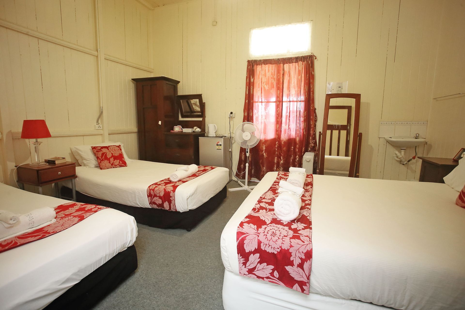 Hotel room with three beds, red accents, and a wardrobe.