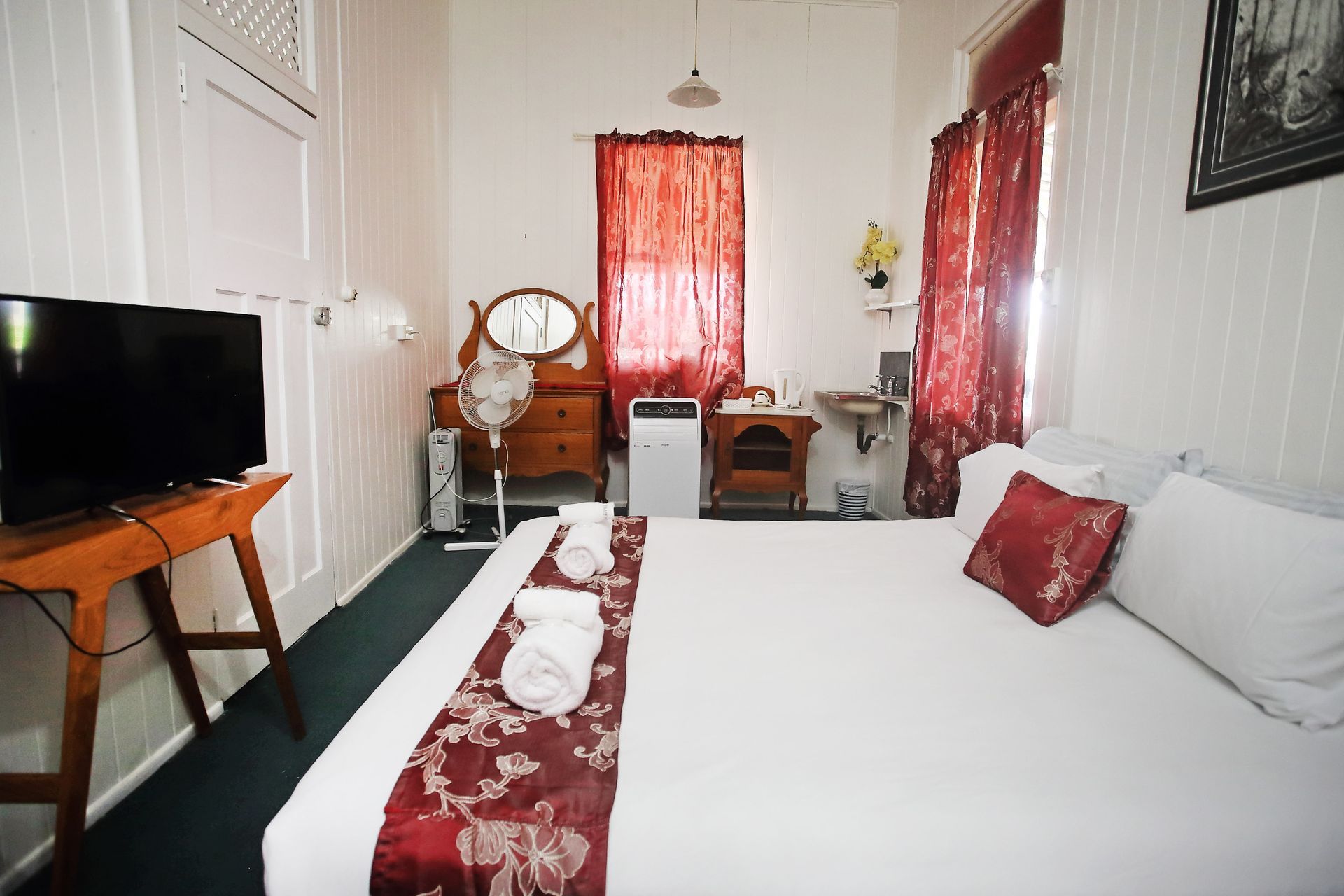 Bedroom with bed, TV, dresser, and small sink; red and white color scheme.