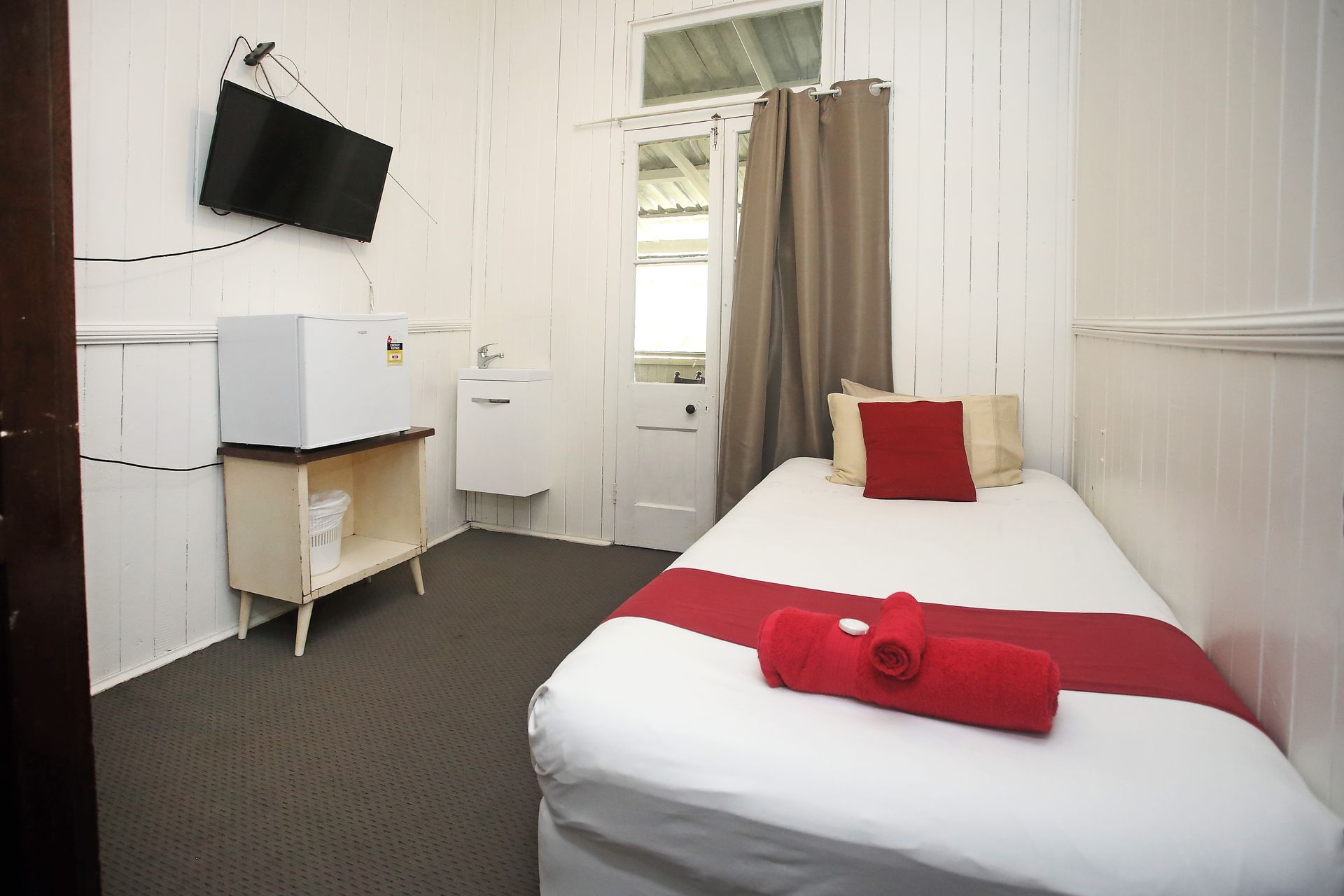 Small, white hotel room with single bed, TV, sink, and open door.