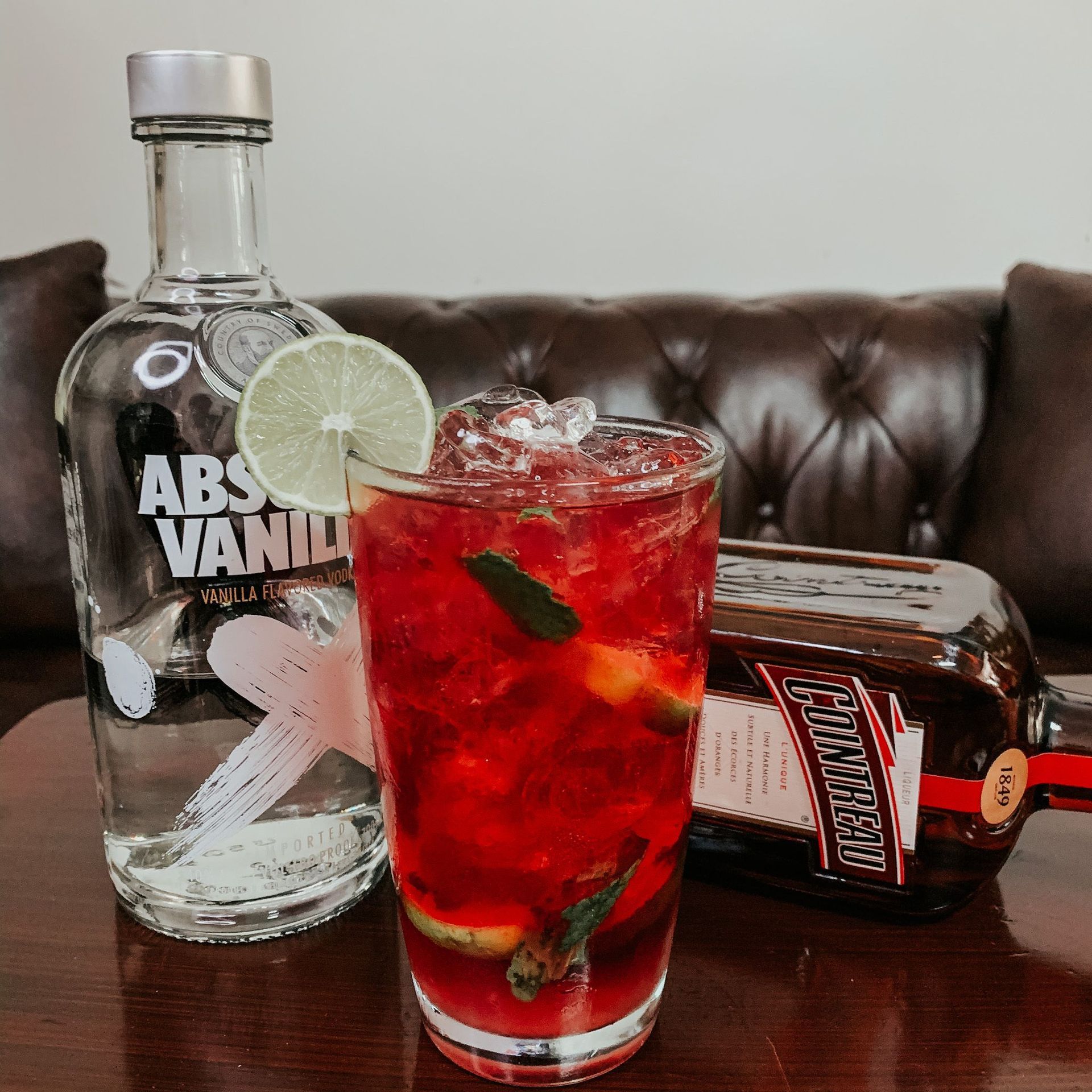 A mixed drink with vodka, garnished with lime and mint, next to two bottles of liquor on a table.