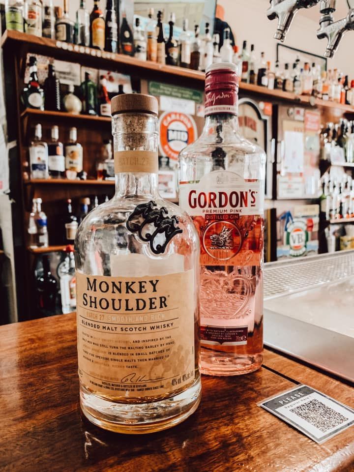 Monkey Shoulder whisky and Gordon's pink gin bottles on a bar counter with a shelf of bottles in the background.