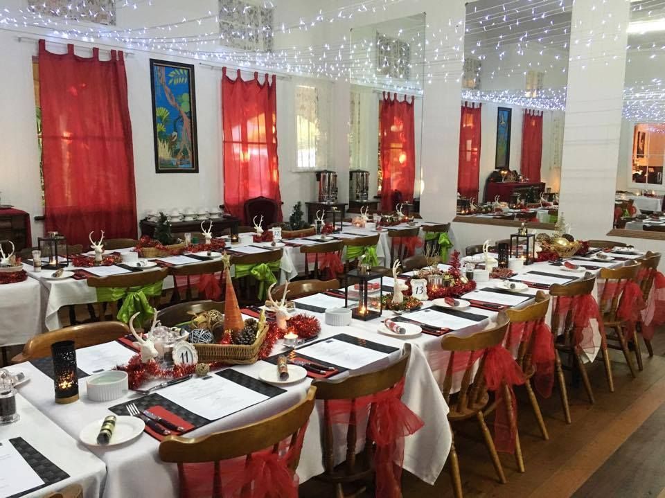 Dining room set for a festive event, with long tables, red decor, and string lights.