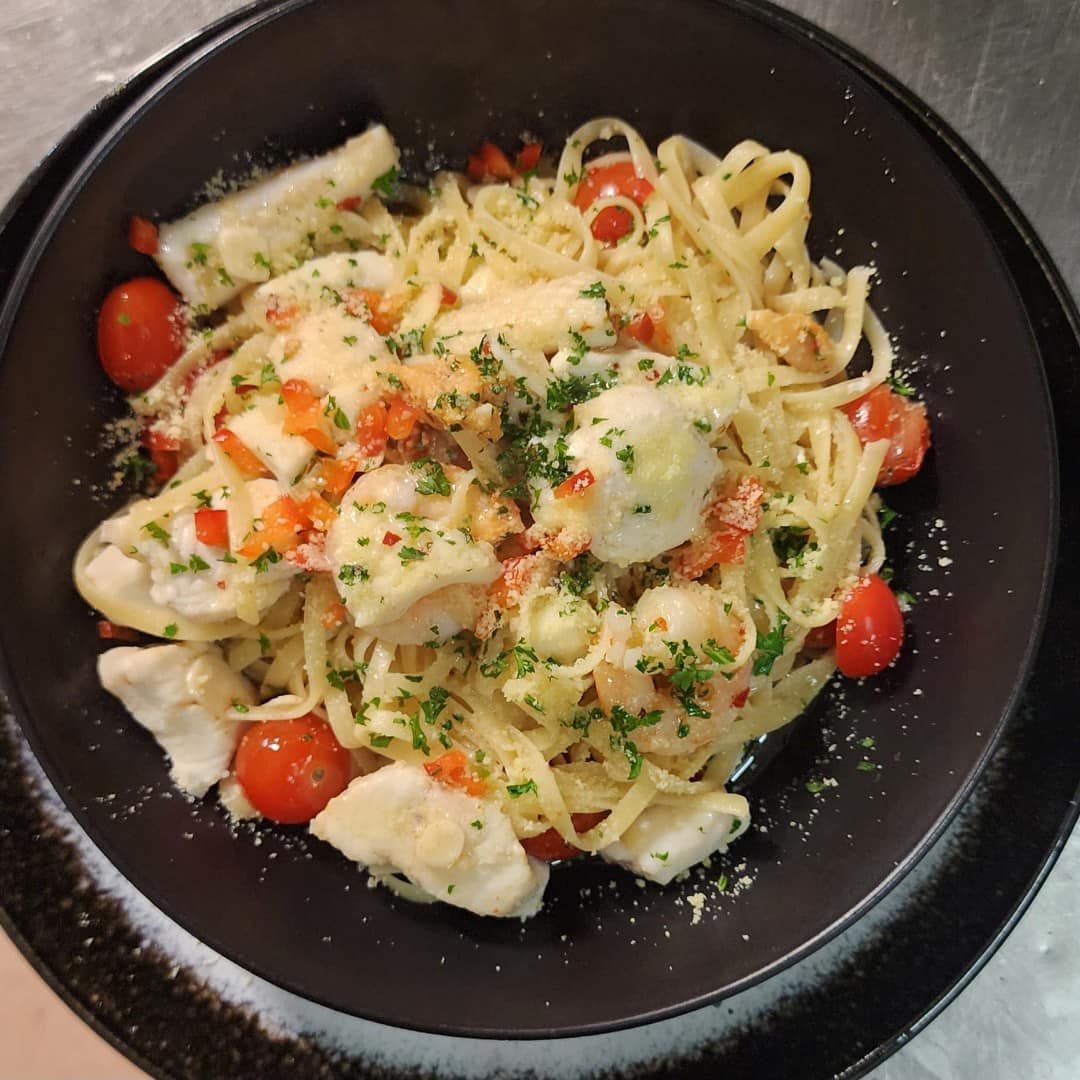 Pasta dish with tomatoes, fish, and herbs in a black bowl.