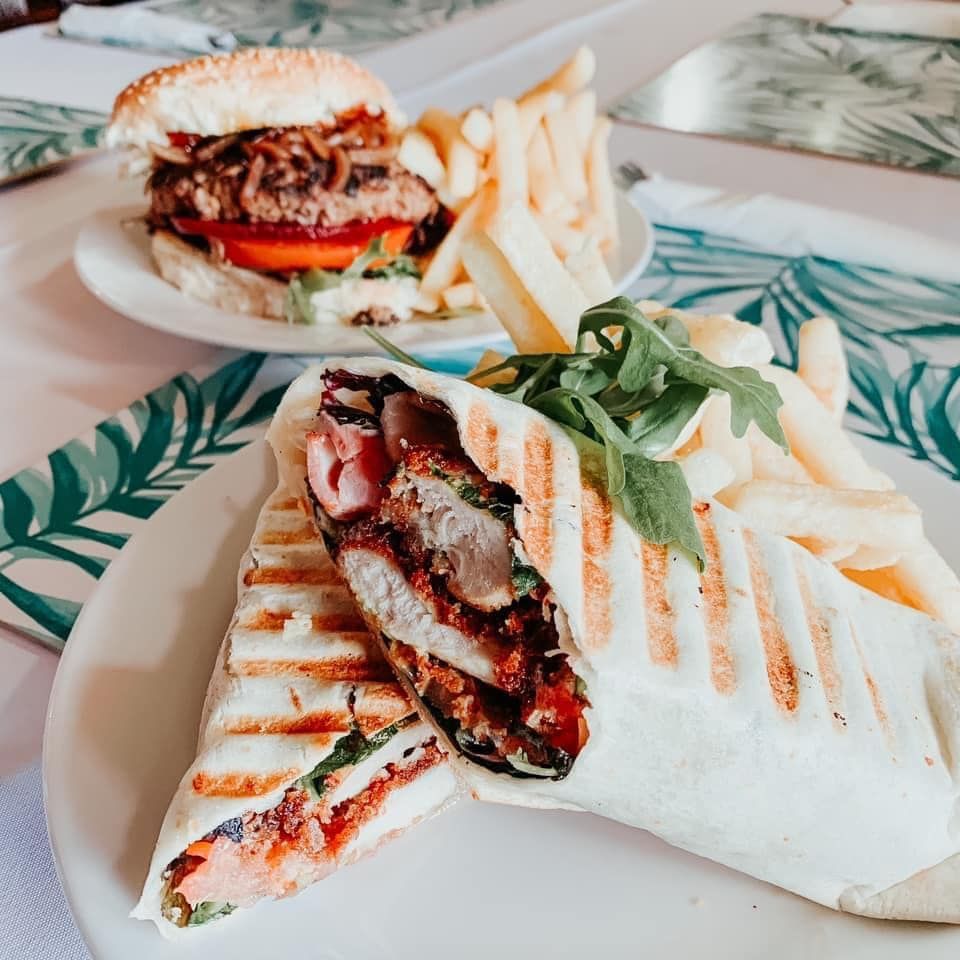 Two plates with food: a burger and a wrap, with fries and greenery.