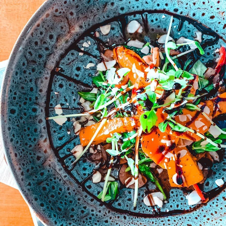 Roasted vegetable salad drizzled with balsamic glaze, sprinkled with nuts, served in a blue bowl.