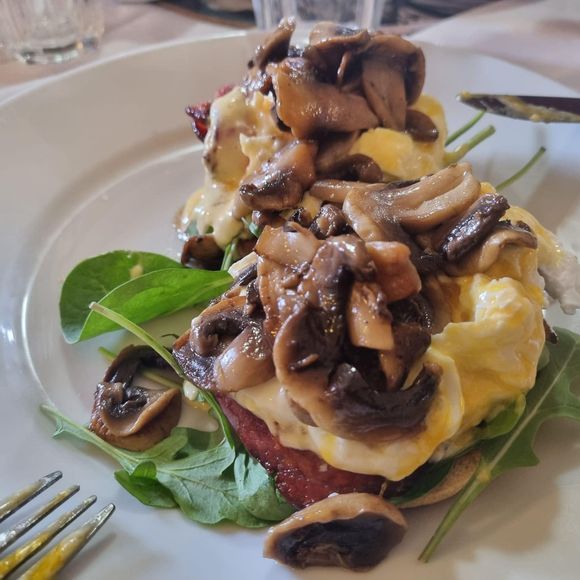 Plate of food: scrambled eggs, mushrooms, bacon, and greens.