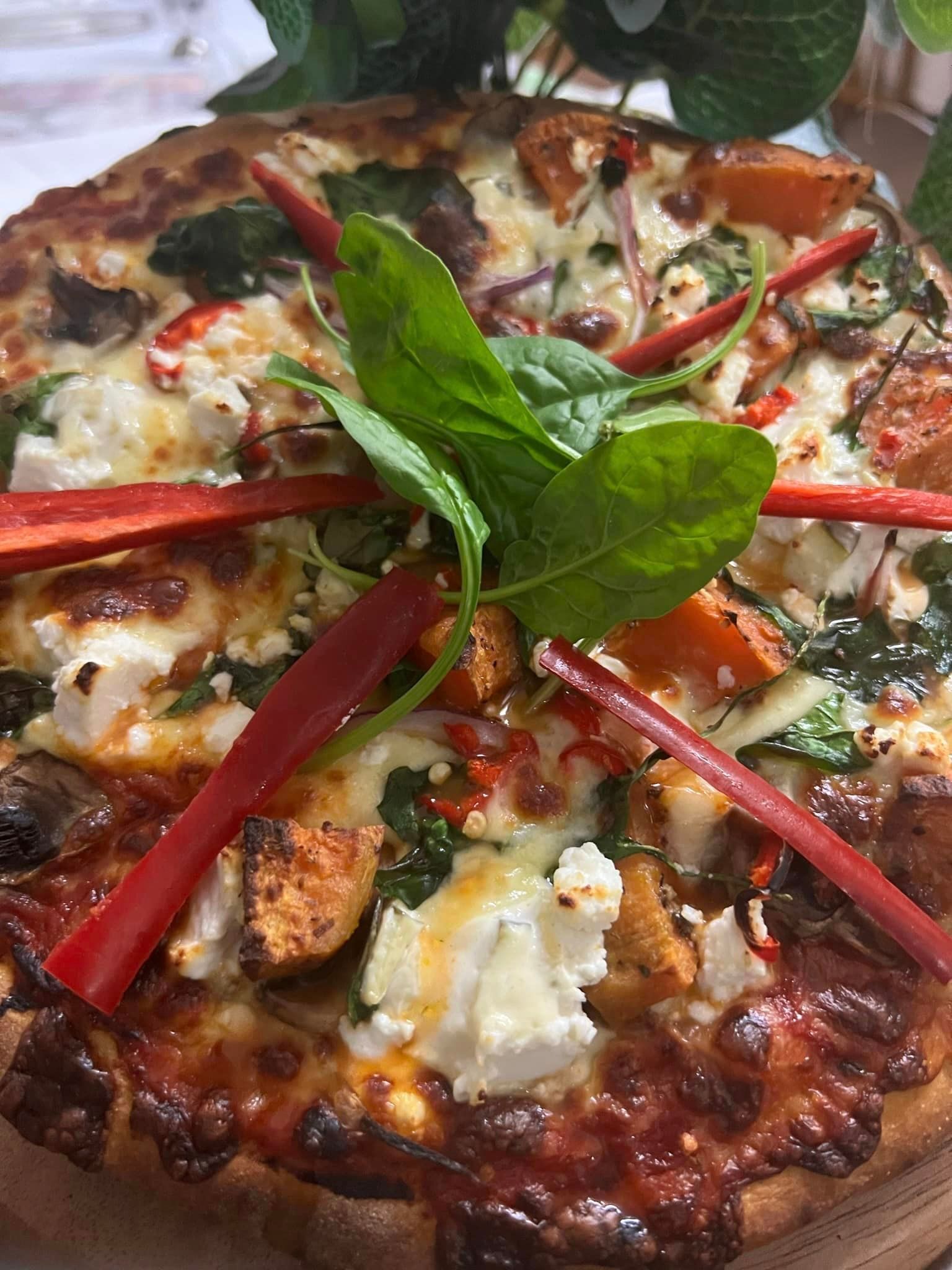 Pizza topped with spinach, tomatoes, cheese, red peppers, and basil.