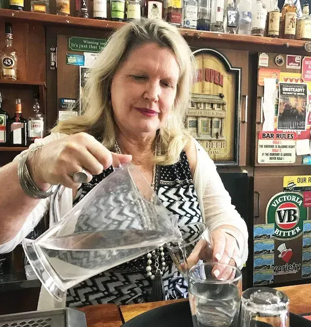 Woman pouring water from a pitcher into a glass at a bar.
